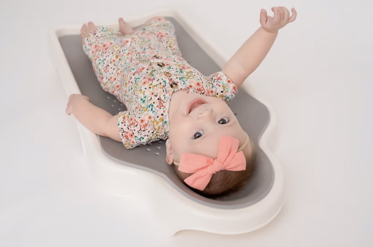 An infant lying on their back on a contoured infant mattress, with the head resting inside a shaped recess in the surface